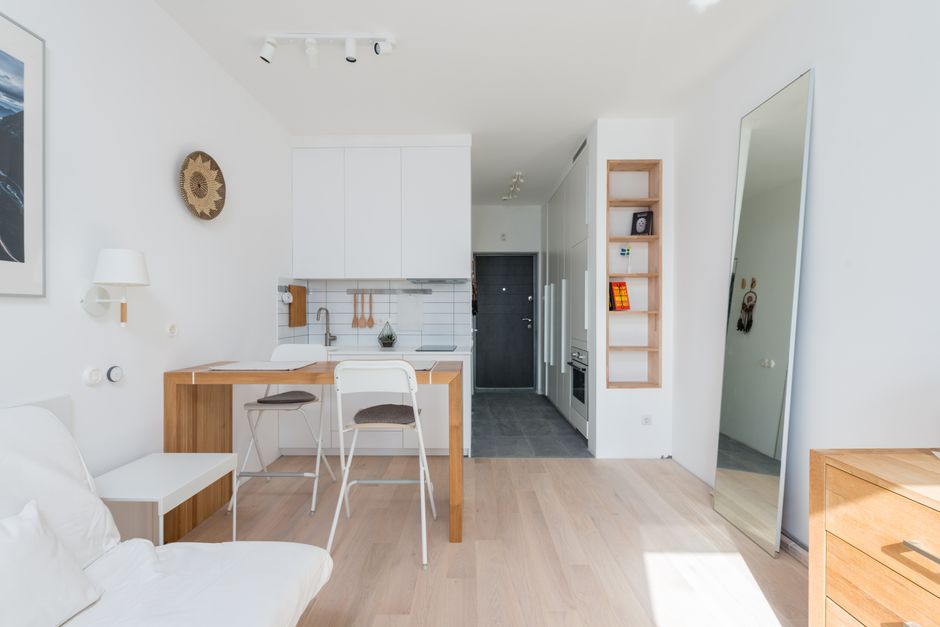 A bright, spacious interior room with white walls and a large window allowing natural light to flood in, situated on an upper floor of a building. The window has a white frame and shows glimpses of ne